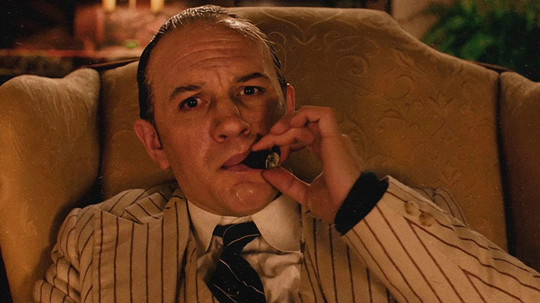 Tom Hardy smoking a cigar and looking into the camera lens as Al Capone in Capone