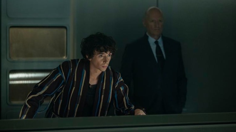 Samuel Blenkin's Boy Kavalier leans in to observe something while Ade Edmonson's Adam Ein stands stoically in the background, in Alien: Earth