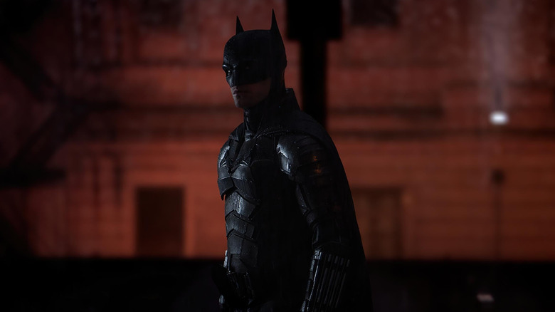 Robert Pattinson as Batman soaked in rain standing in the streets of Gotham in The Batman