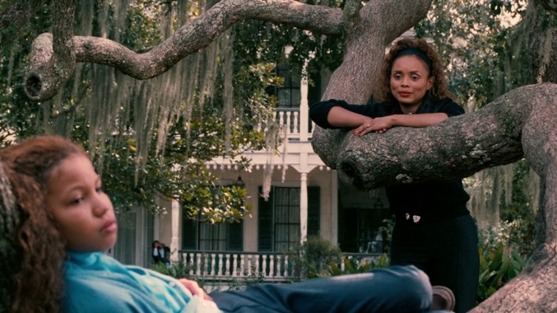 Jurnee Smollett as Eve Batiste lying on the ground while Debbi Morgan as Mozelle Batiste Delacroix watches her from behind a tree in Eve's Bayou