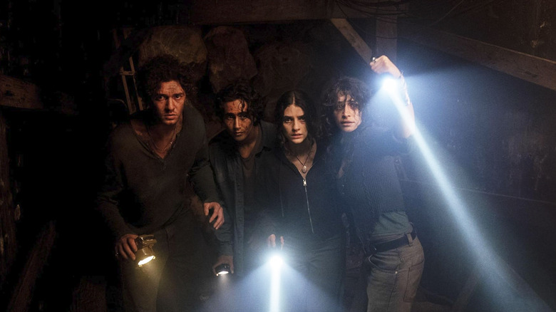 The cast of Until Dawn huddled together wielding flashlights in an underground tunnel