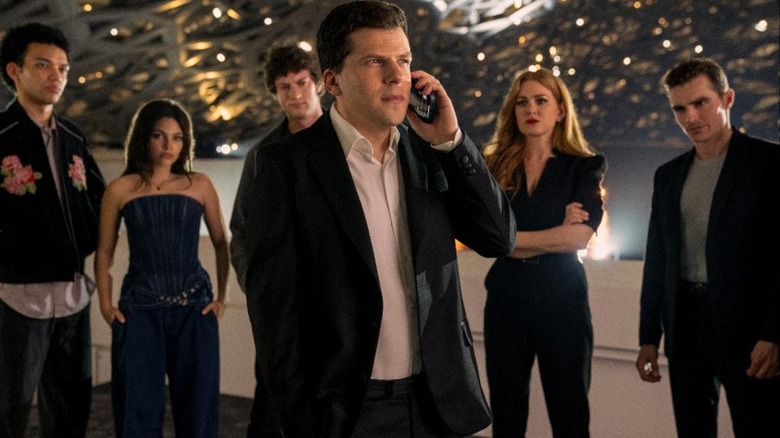 Jesse Eisenberg as J. Daniel Atlas, Isla Fisher as Henley Reeves, and Dave Franco as Jack Wilder standing in front of an art installation in Now You See Me: Now You Don't