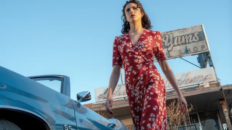 Margaret Qualley emerges from a car in a red floral-print dress in Honey Don't!