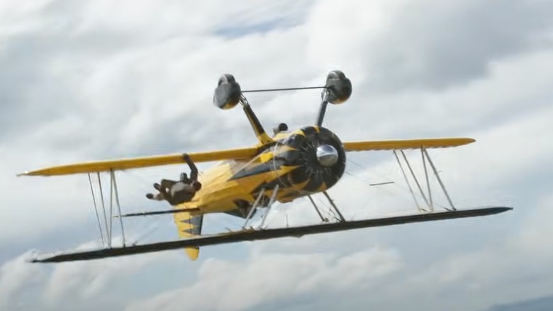 Ethan Hunt (Tom Cruise) hangs on the side of a biplane wing as it flies upside down through a cloudy sky