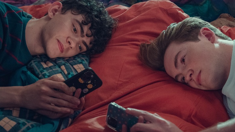 Joe Locke's Charlie and Kit Connor's Nick lay opposite one another, looking at their respective phones, in Heartstopper