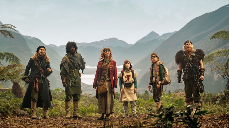 The Time Bandits, dressed in eclectic garb, stare up at the horizon while standing amidst a forest scene in 