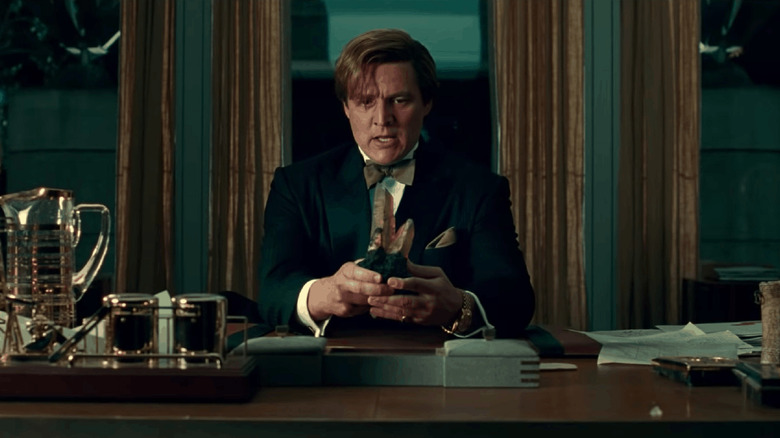 Maxwell Lorenzano holding a magical wishing stone at his desk in Wonder Woman 1984