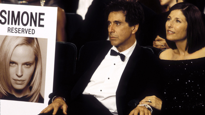 Viktor Taransky (Al Pacino), in a tuxedo, sitting next to a poster of Simone (Rachel Roberts) with Elaine Christian (Catherine Keener) in S1m0ne