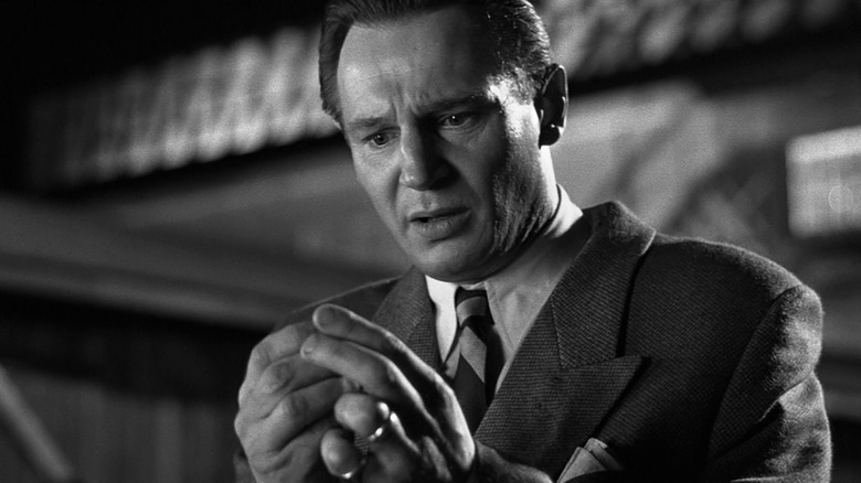 Oskar Schindler looking at something in his fingers in Schindler's List