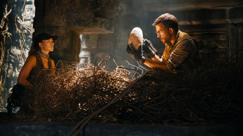 Scarlett Johansson as Zora Bennett crouching beside a nest as Jonathan Bailey as Dr. Henry Loomis holds up an egg in Jurassic World Rebirth
