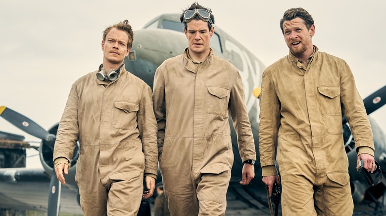 Alfie Allen, Connor Swindells and Jack O'Connell in overalls walking away from a plane