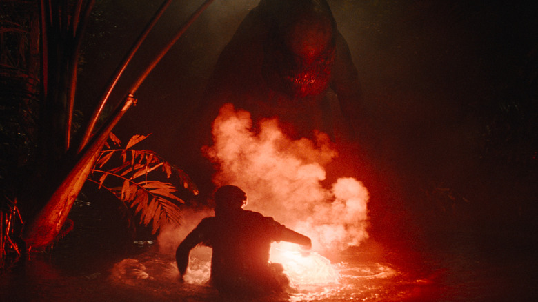 Mahershala Ali as Duncan Keith holding a red flare and facing off against a D-Rex in Jurassic World Rebirth