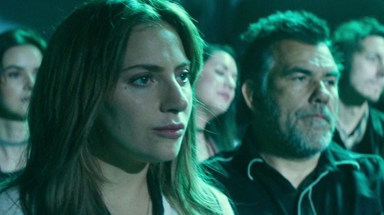 Lady Gaga as Ally, lit green, standing at the side stage in A Star Is Born