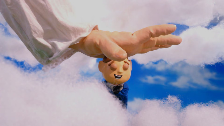 The hand of God pats a smiling Orel on the head as he floats amongst the clouds with a blue sky behind him in "Moral Orel"