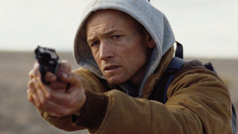 She Rides Shotgun - Nate (Taron Egerton) holding a revolver