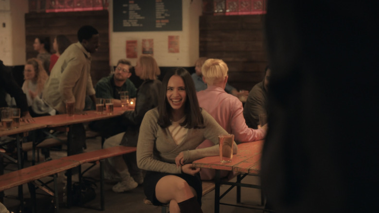 Sofia Carson as Anna De La Vega laughs as she watches Corey Mylchreest as Jamie Davenport perform karaoke in My Oxford Year
