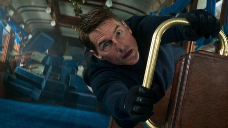 Tom Cruise as Ethan Hunt holding on as a train falls behind him, in Mission: Impossible - Dead Reckoning, Part One